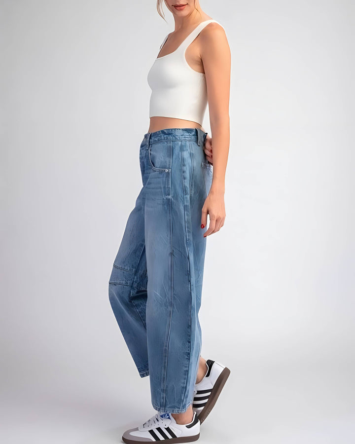 A model wearing light blue wide-leg cropped jeans, a white crop top, and white sneakers with black stripes, standing against a light gray studio background.
