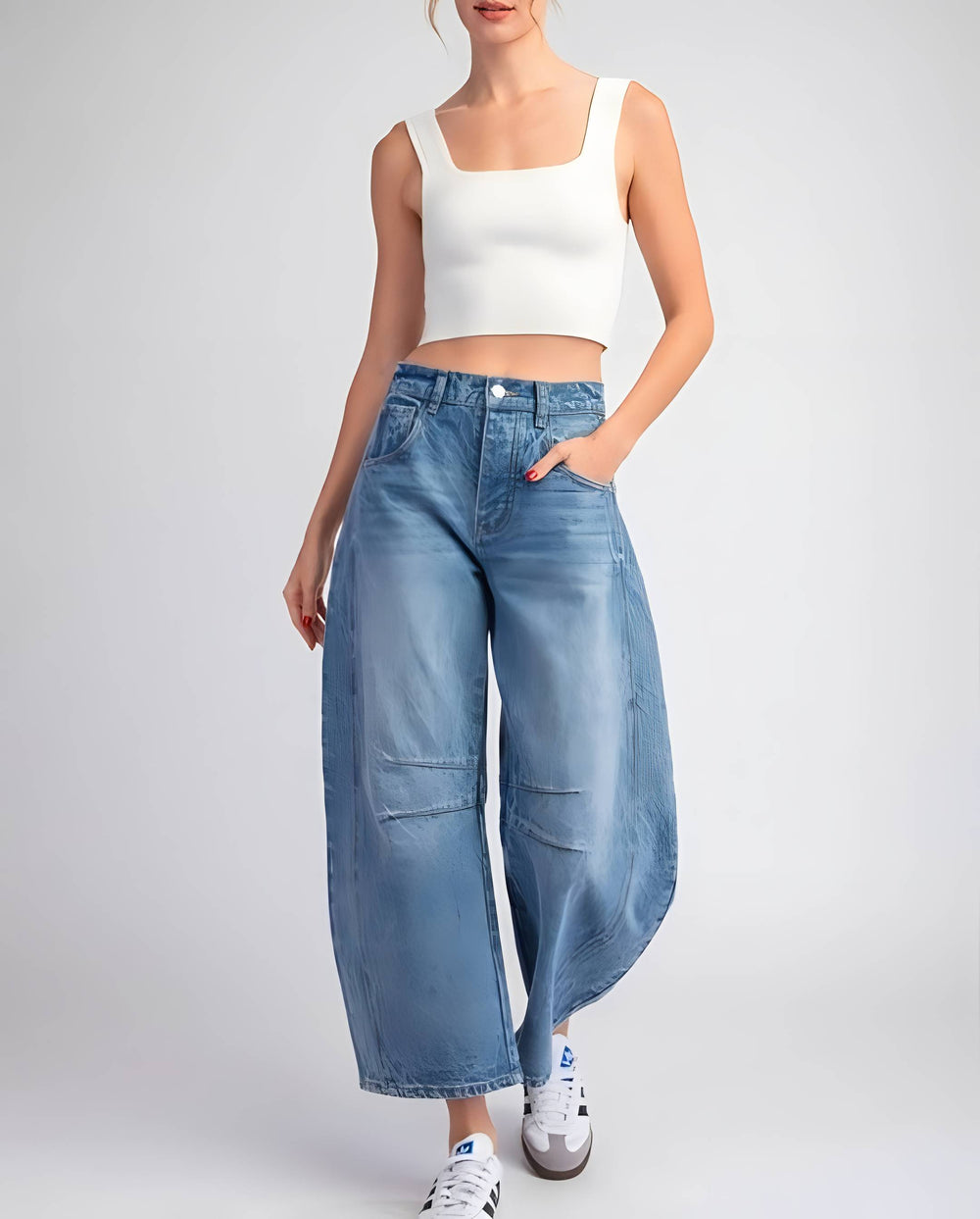A model wearing light-wash blue wide-leg cropped jeans, a white ribbed crop top, and white sneakers, standing against a light gray studio background.