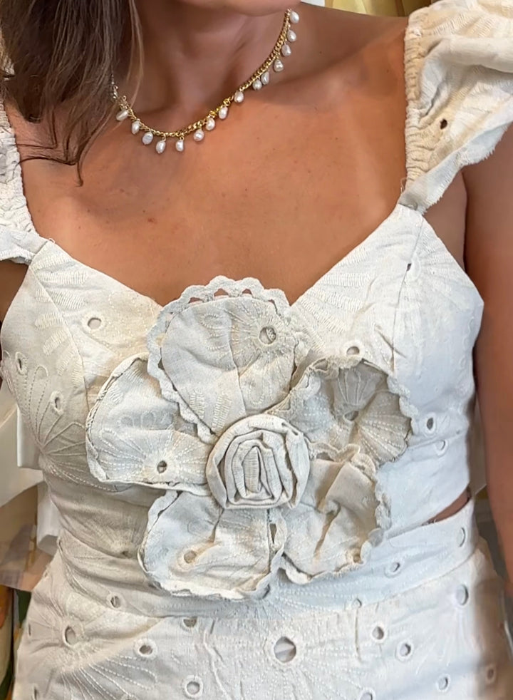 Close-up of a white floral dress with intricate details and a pearl necklace.