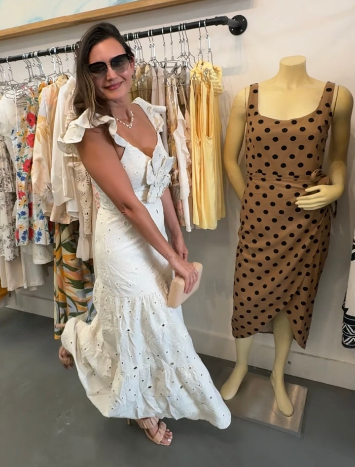 Woman in a white dress standing next to a mannequin wearing a polka dot dress in a clothing store.
