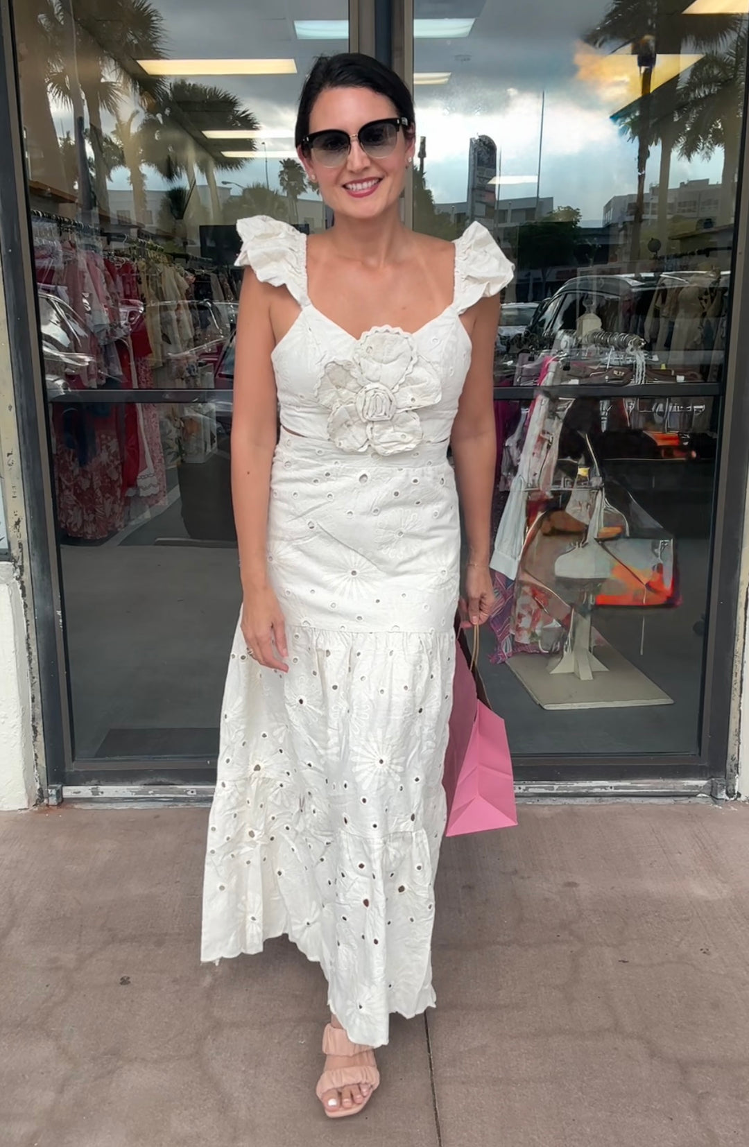 Woman in a white dress standing outside a store with palm trees in the background