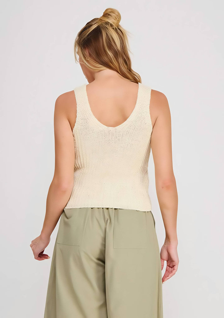 Woman wearing a beige sleeveless top and light green pants on a white background