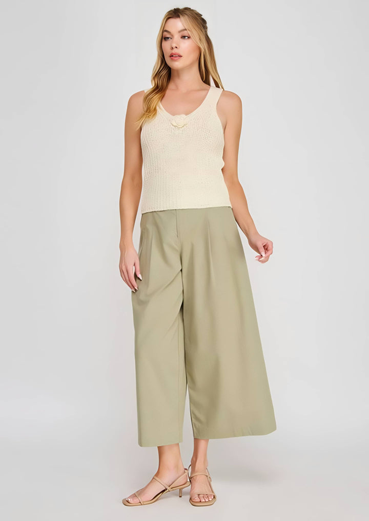 Woman wearing a beige sleeveless top and green wide-leg pants on a white background