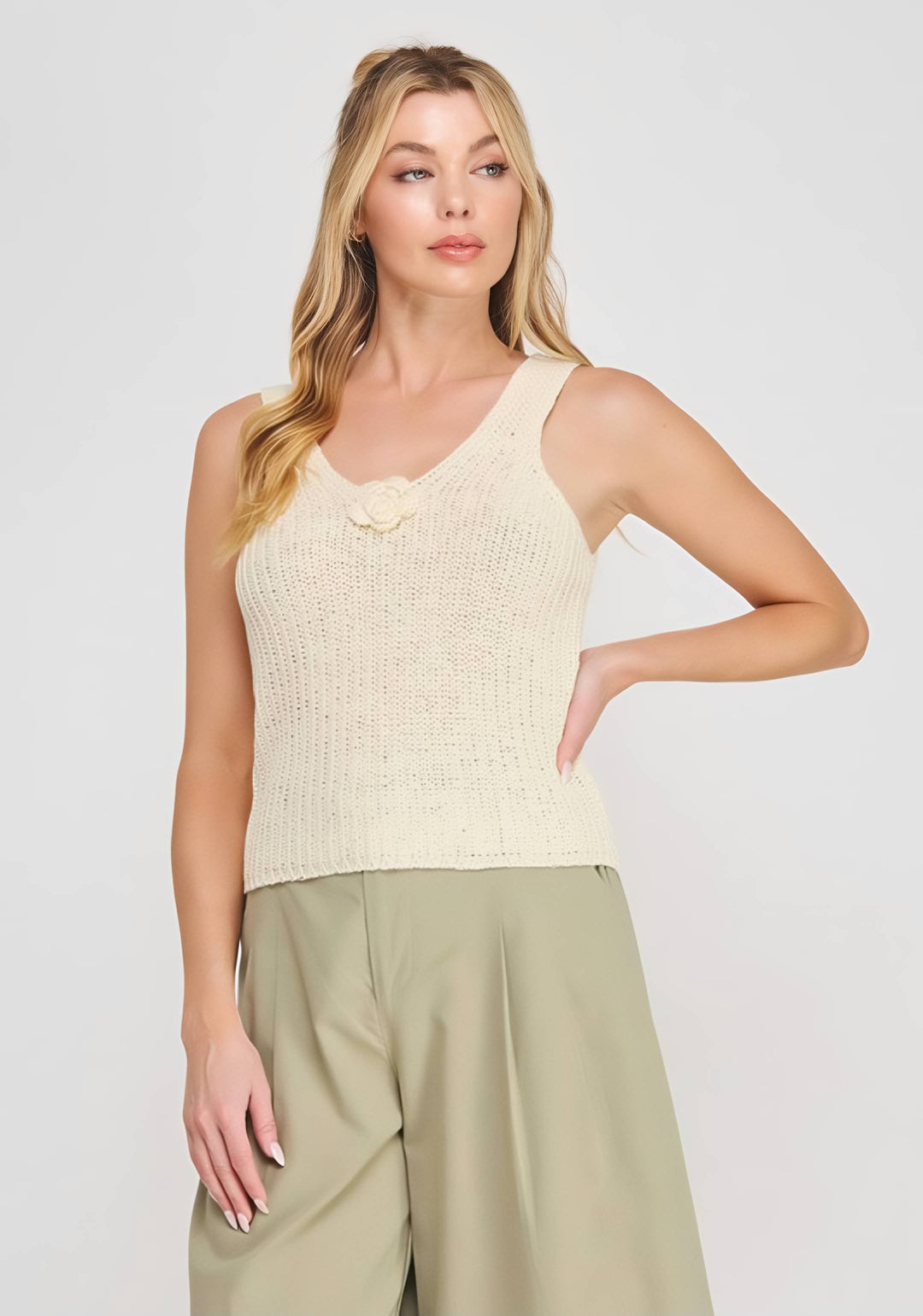 Woman wearing a beige sleeveless top and beige pants against a white background