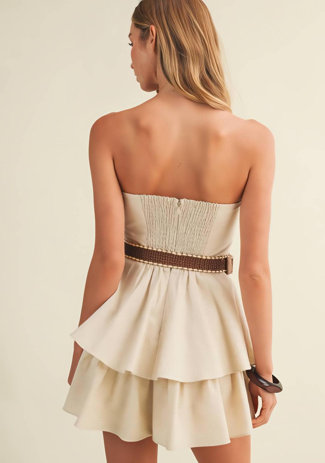 Woman wearing a strapless beige dress with a brown belt on a plain background