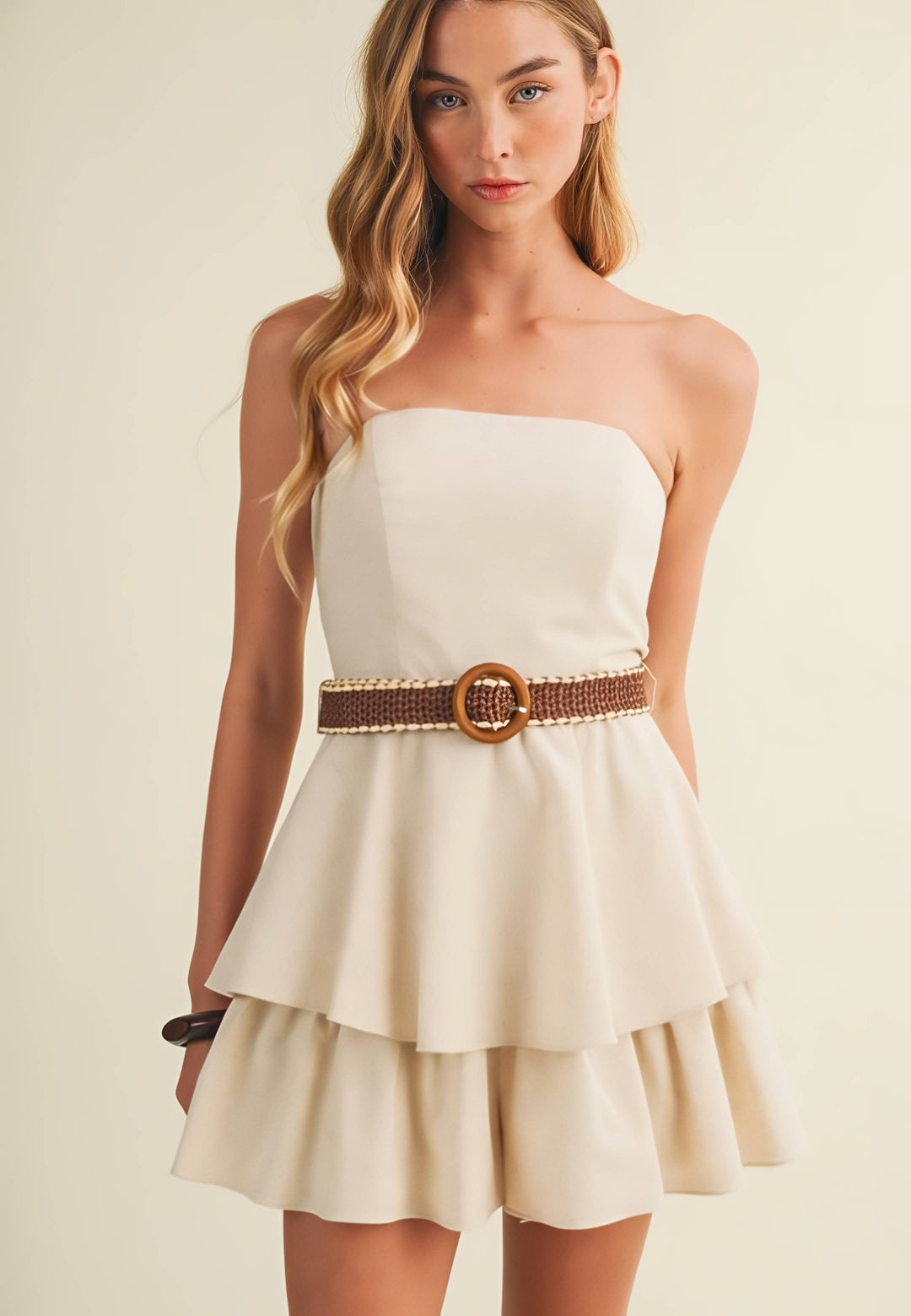 Woman wearing a strapless beige romper/dress with a brown belt on a beige background