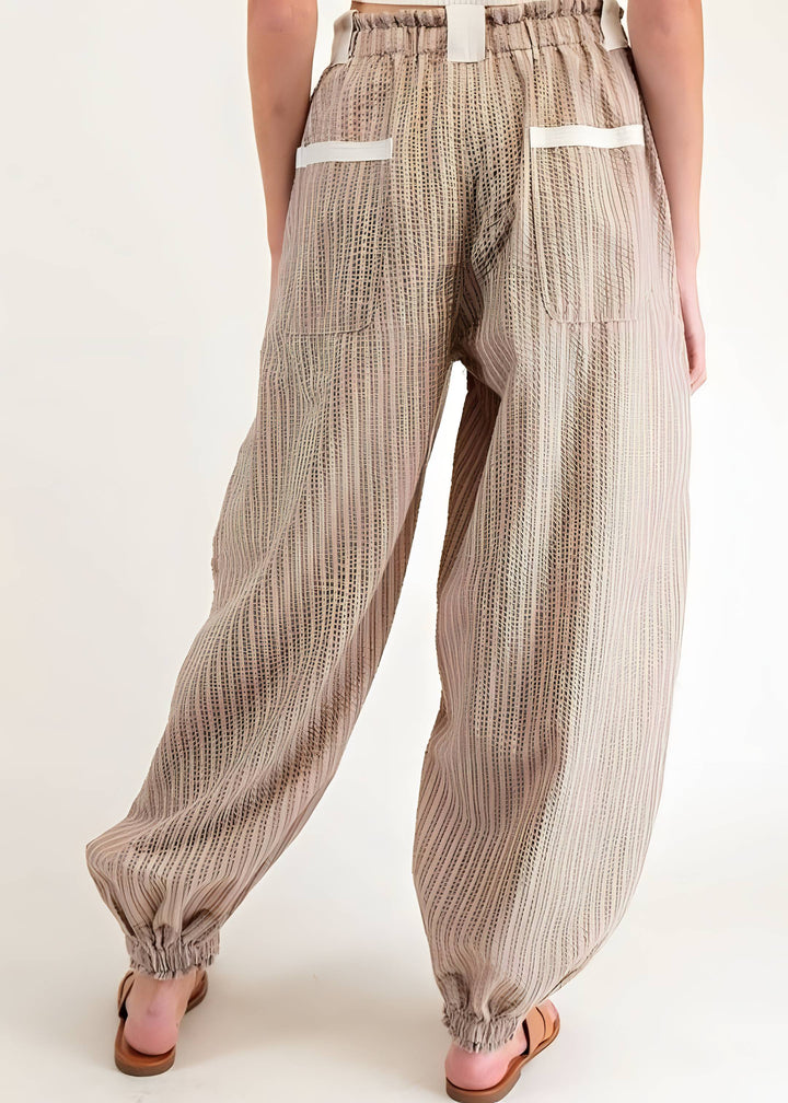 A person shown from the back wearing loose, wide-leg beige pants with vertical darker stripes, elastic waistband, and elastic ankle cuffs. The photo is cropped from the waist down on a plain light background.