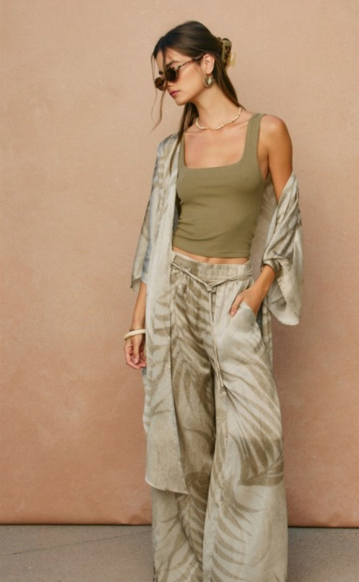 Woman wearing a green top and patterned pants against a beige wall