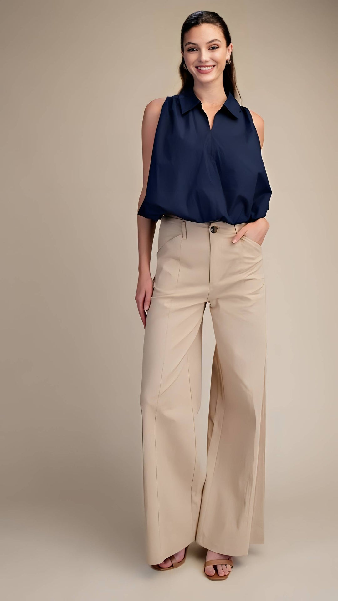 Woman wearing a navy sleeveless top and beige wide-leg pants on a beige background
