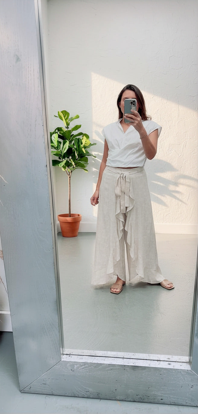 Person taking a mirror selfie wearing a white top and beige skirt in a room with a plant.