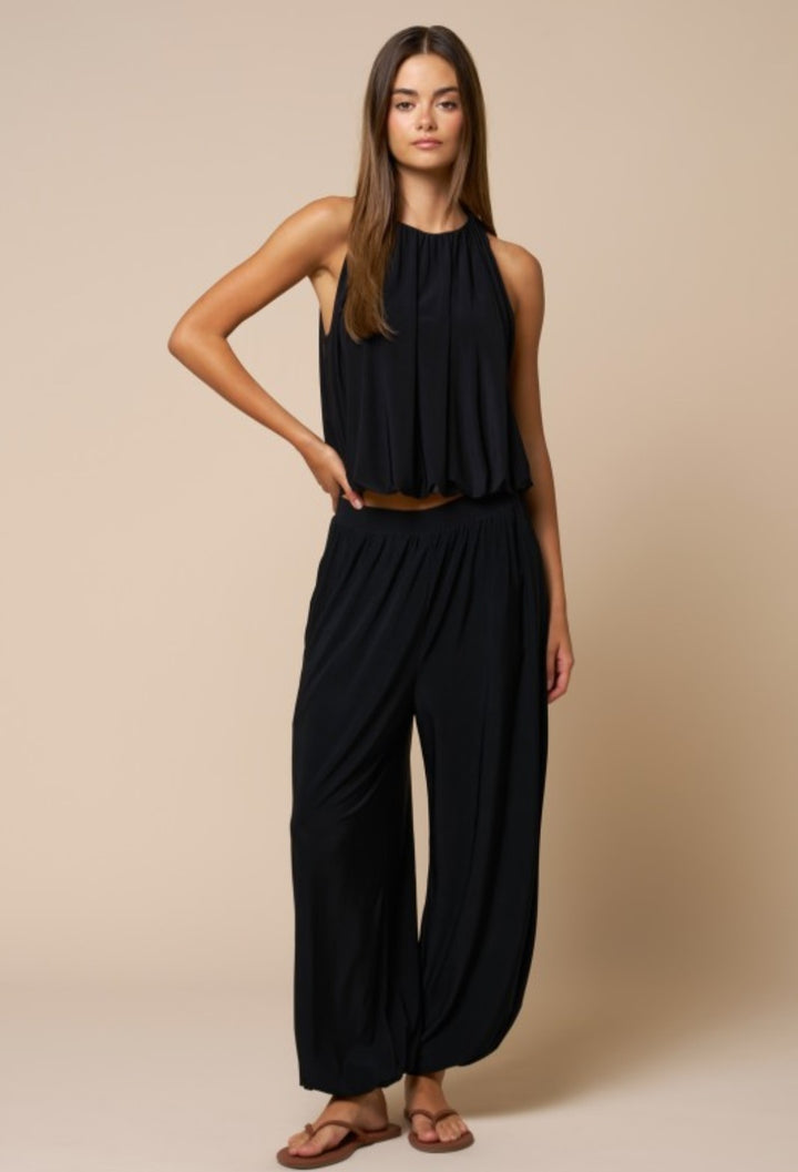 Woman wearing a black sleeveless top and wide-leg pants against a beige background