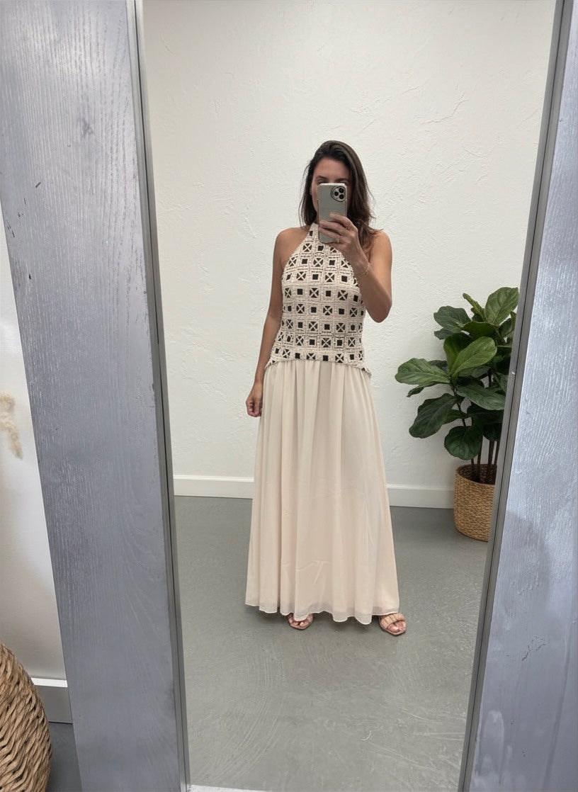 Woman taking a mirror selfie wearing a long dress with intricate top and plain bottom.