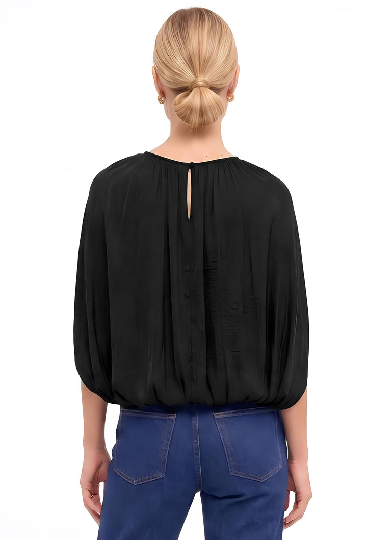 A woman viewed from the back wearing a black long-sleeve blouse with a small center back slit and blue jeans, against a plain white background.