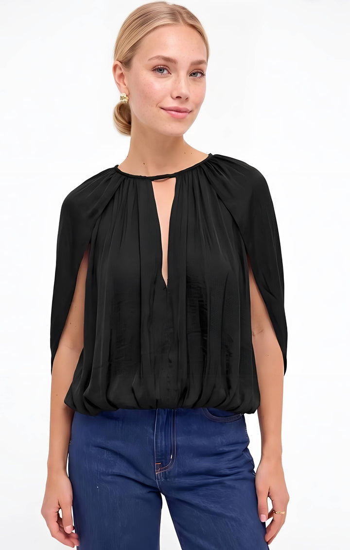 A woman wearing a black draped cap-sleeve blouse with a keyhole neckline and blue jeans, photographed against a plain white studio background.