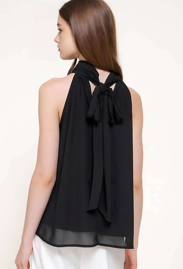 A woman shown from the back wearing a black sleeveless halter-style top with a large bow at the back and white bottoms, against a plain light background.