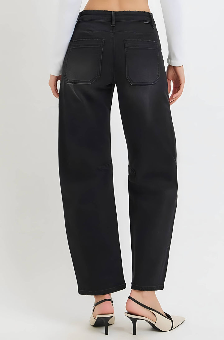 Rear view of a model wearing black wide-leg cropped jeans with back patch pockets, paired with a white long-sleeve top and black-and-cream slingback heels, against a light gray studio background.