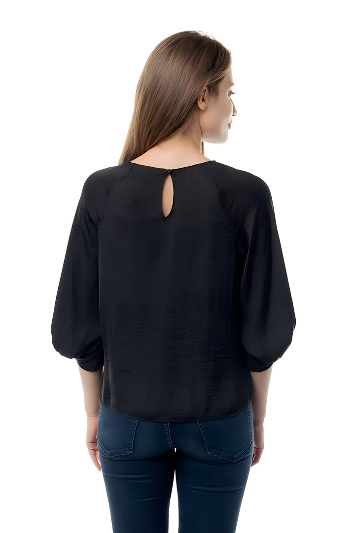 A woman viewed from the back wearing a black long-sleeve blouse with a small keyhole cutout at the neckline, paired with dark blue jeans, against a plain white background.