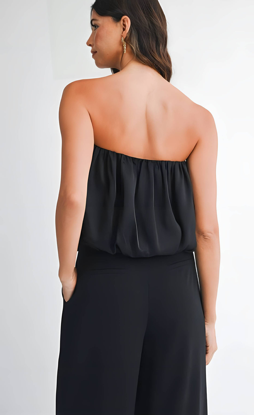 Woman wearing a black strapless top and high-waisted pants on a plain background