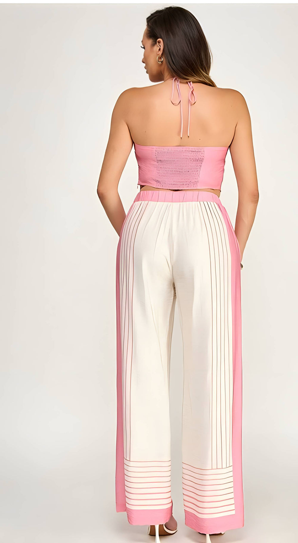 Woman wearing a pink and white outfit with a strapless top and wide-leg pants on a white background