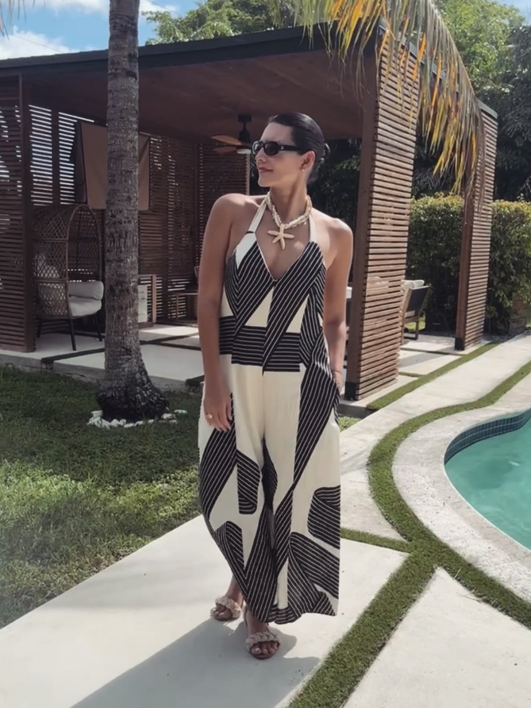 Woman in a black and white patterned dress standing by a poolside.