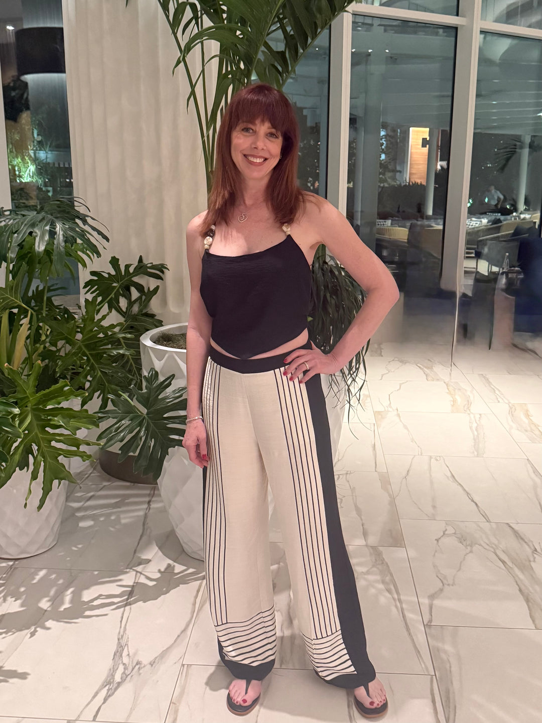 Woman posing in a stylish outfit with wide-leg pants and a crop top in an indoor setting.