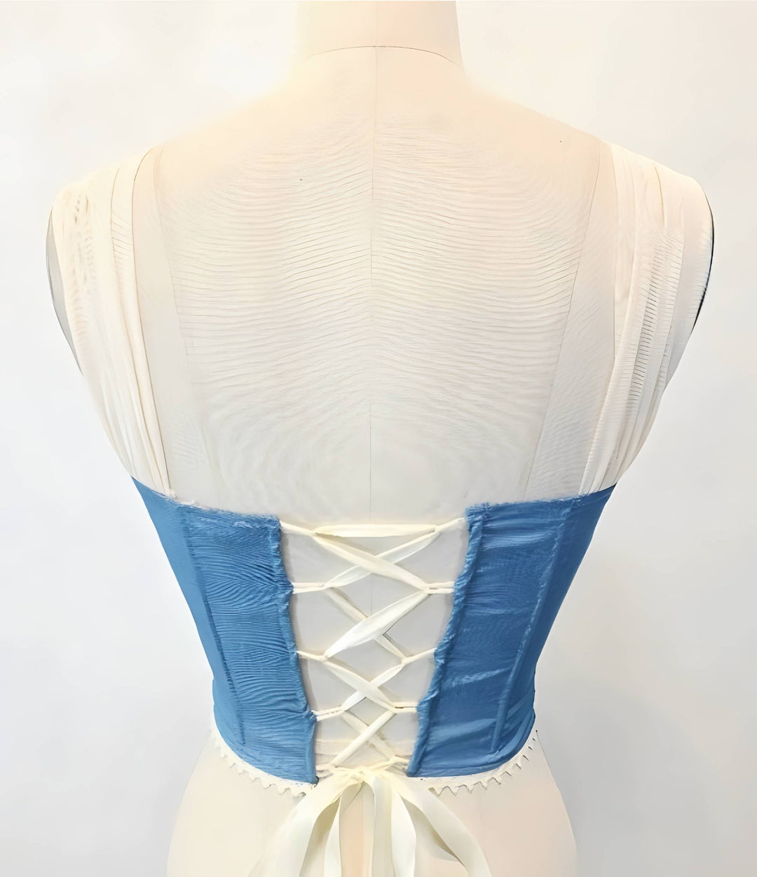 Mannequin wearing a white dress with blue lace details on a plain background