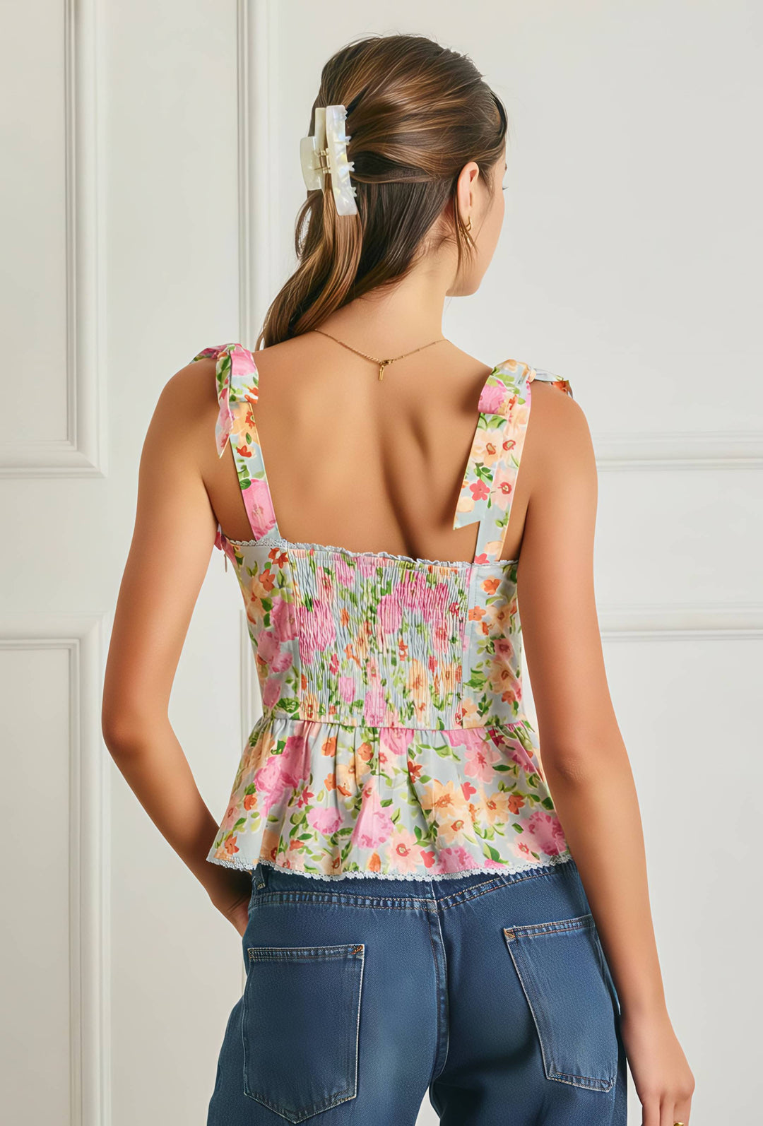 Woman wearing a floral top and blue jeans against a white wall