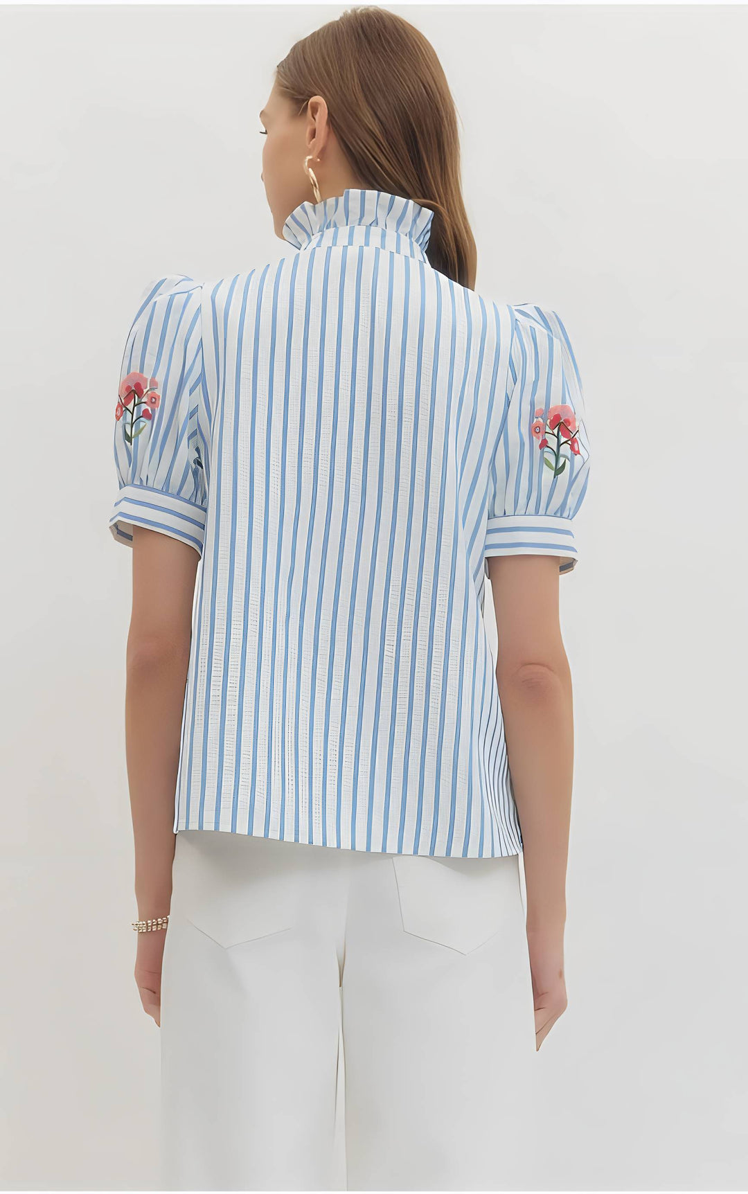 Woman wearing a blue and white striped shirt with floral embroidery on a plain background