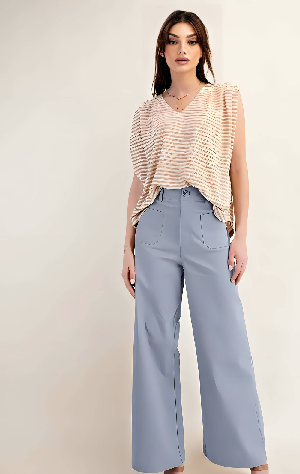 Woman wearing a beige striped top and light blue high-waisted pants on a plain background
