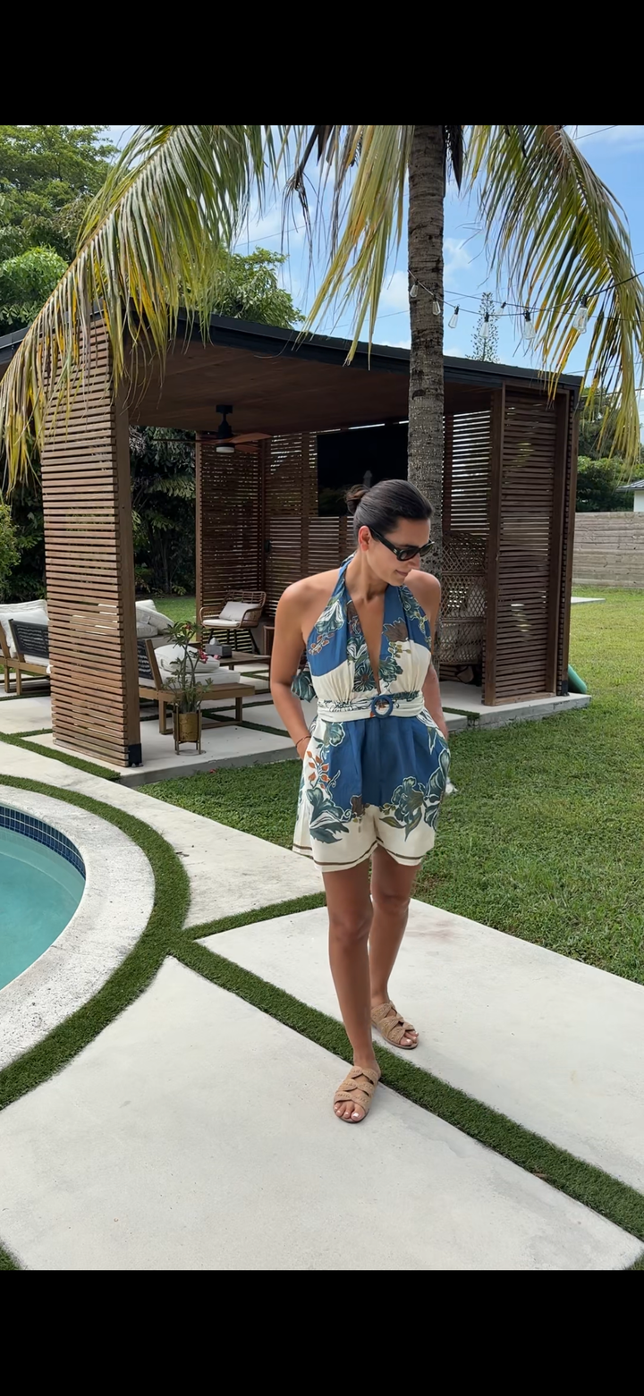 Woman in a blue and white patterned romper standing by a pool with palm trees in the background