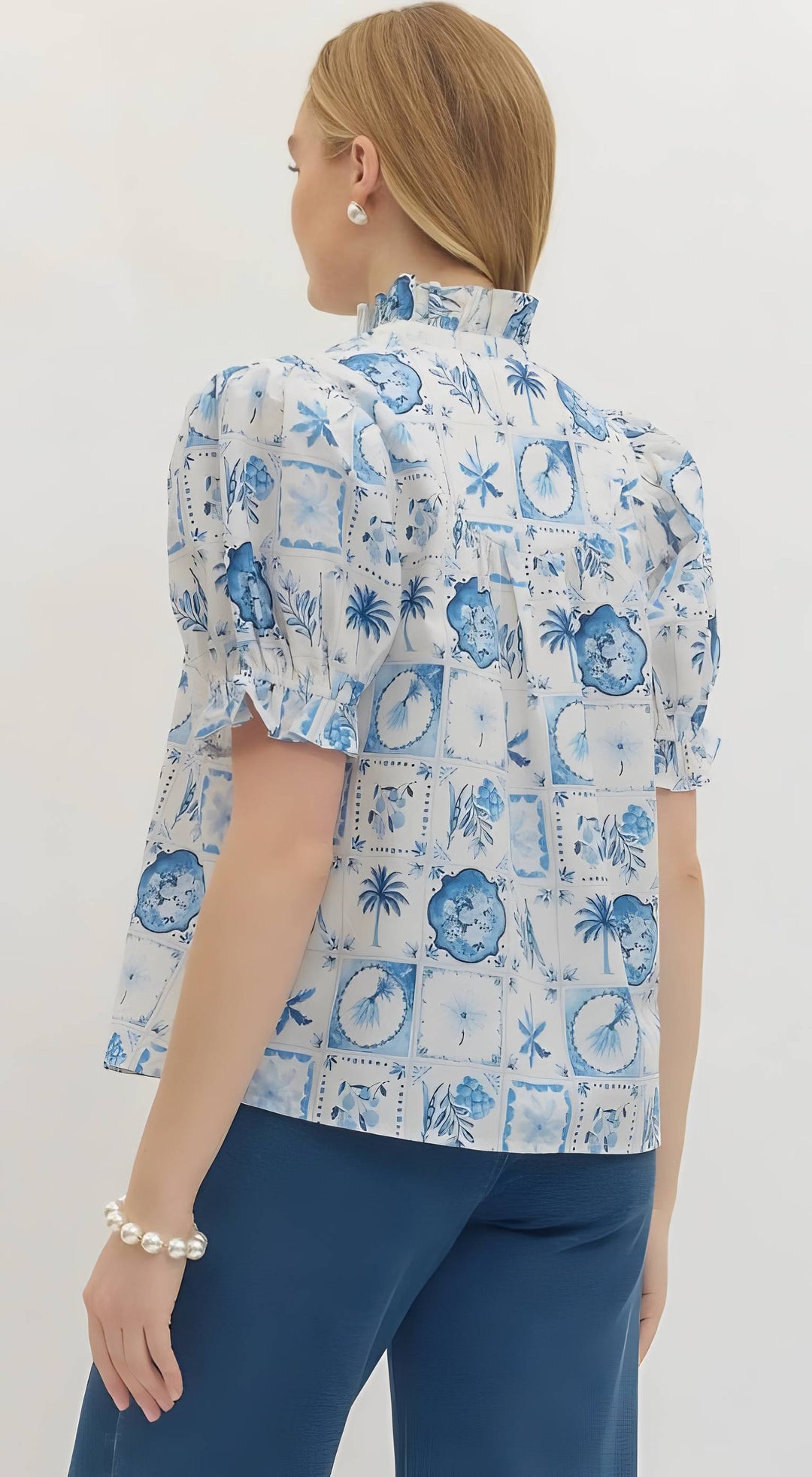Woman wearing a blue and white patterned blouse with blue pants on a white background