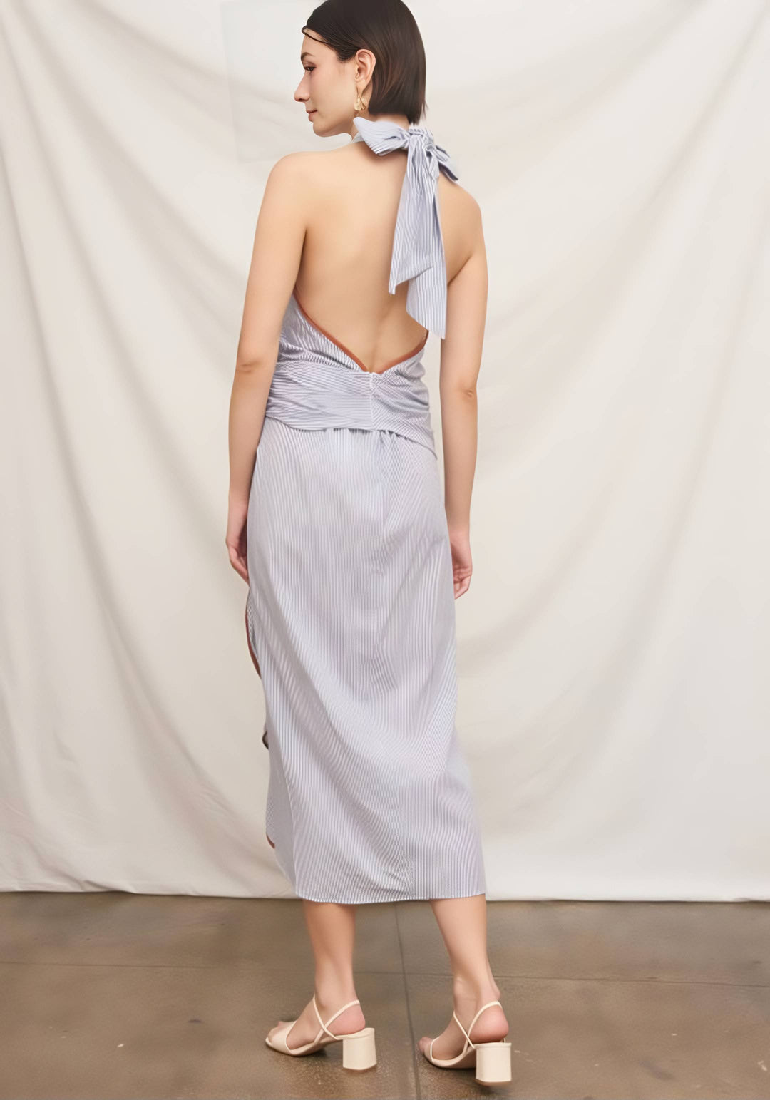 Woman wearing a light purple dress with a backless design and a scarf around her neck, standing against a plain white background.