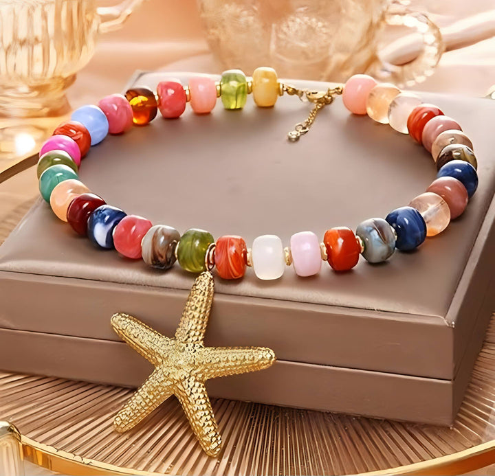 A multicolor beaded necklace with a textured gold starfish pendant, displayed on a brown jewelry box.
