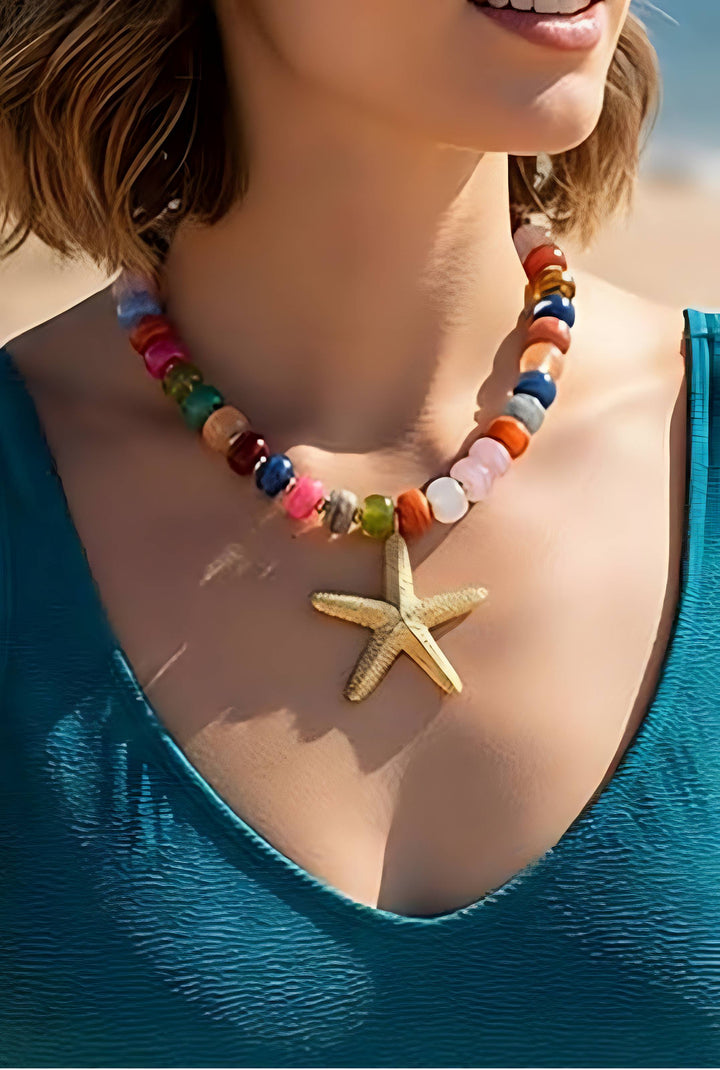 A close-up lifestyle shot of a woman wearing a colorful beaded necklace with a gold starfish pendant, paired with a teal blue top.
