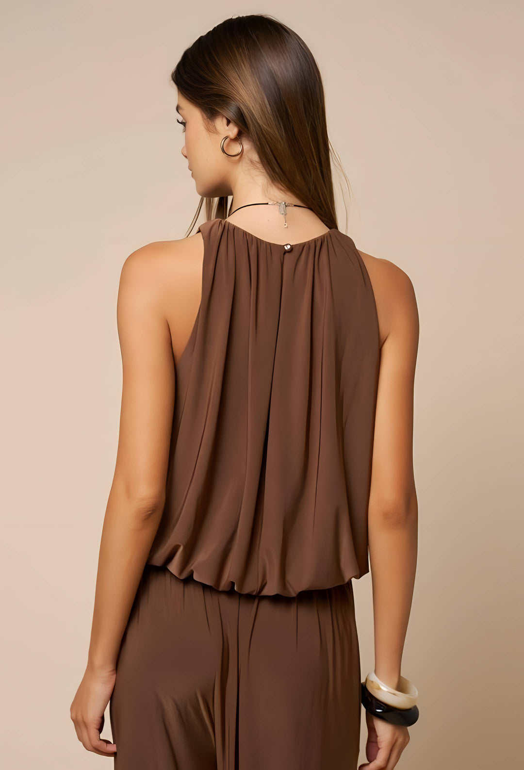 A woman shown from the back wearing a sleeveless draped brown top and matching brown bottoms against a plain beige studio background.