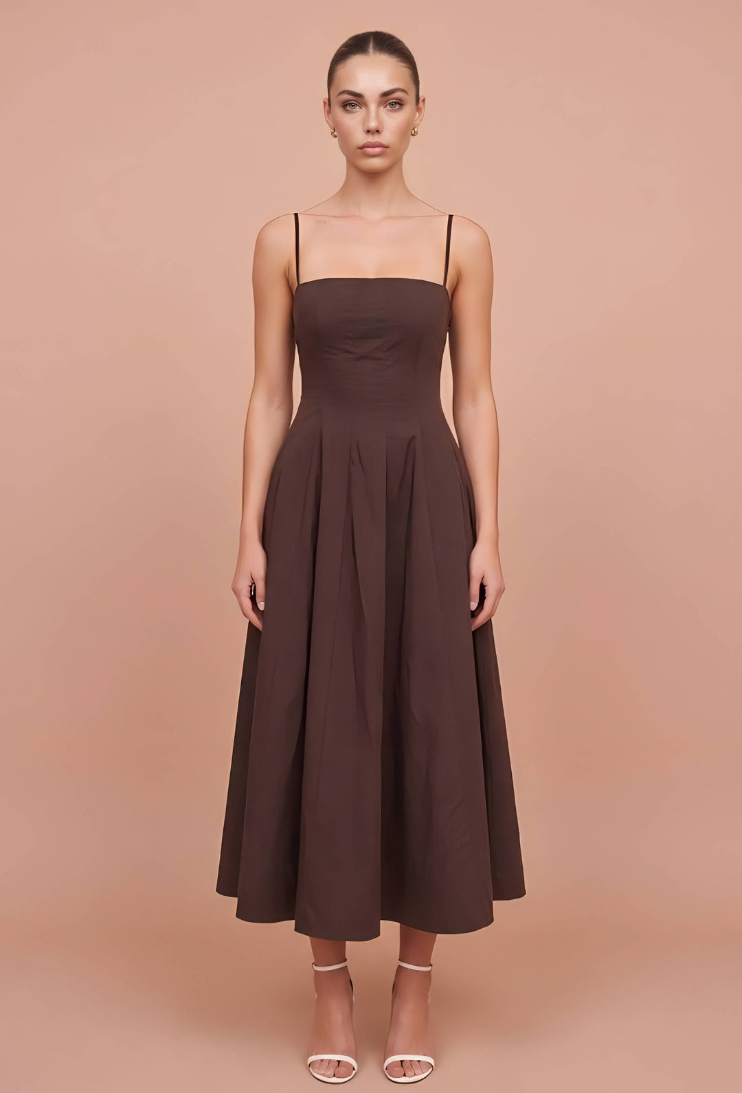 A woman modeling a dark brown midi dress with thin spaghetti straps, a square neckline, a structured bodice, and a flared skirt, set against a solid peach studio background.
