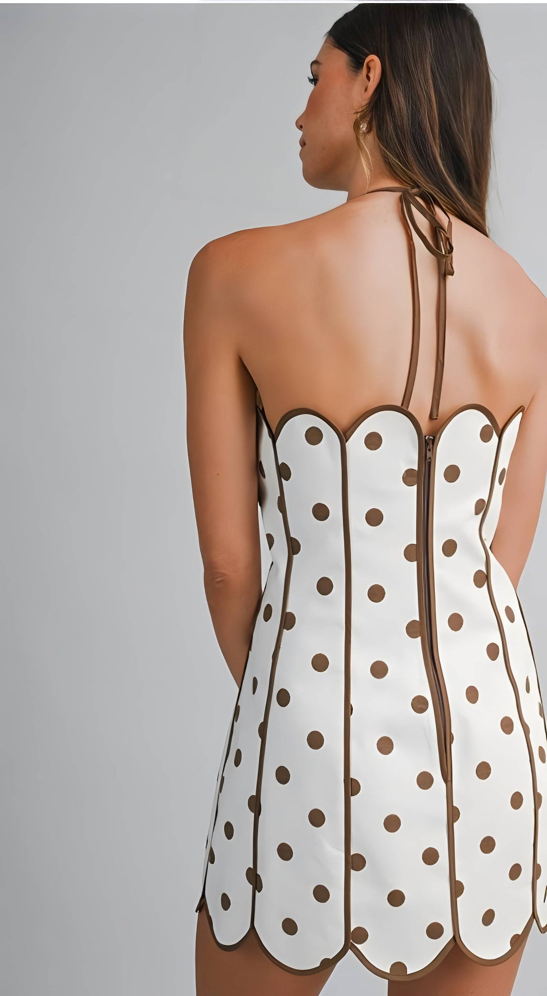Woman wearing a white dress with brown polka dots and thin straps on a gray background