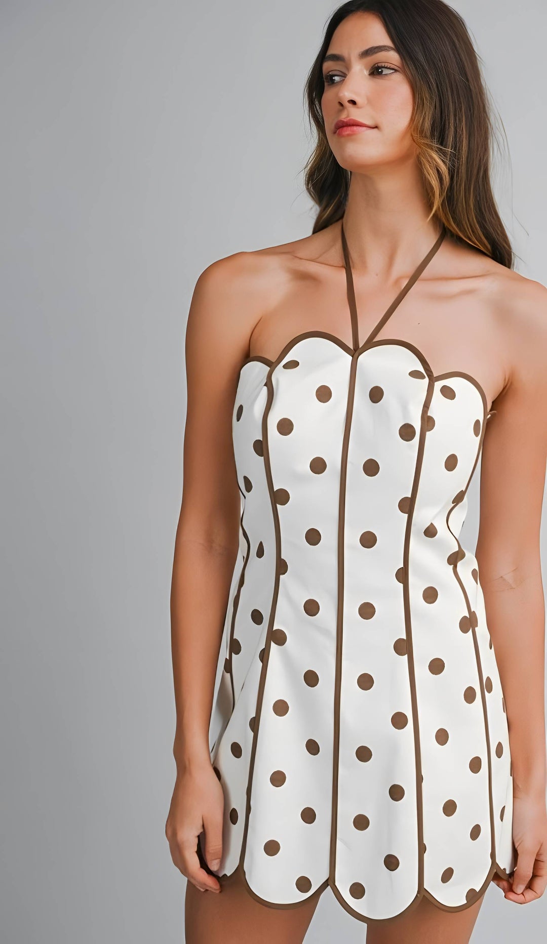 Woman wearing a white dress with brown polka dots against a gray background