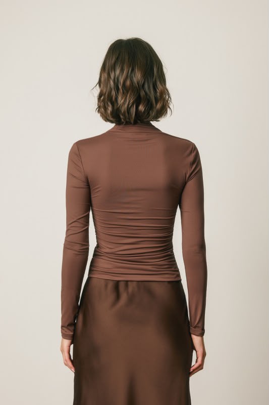 A woman viewed from the back wearing a fitted, long-sleeve brown mock-neck top and a matching brown skirt against a plain light beige background.