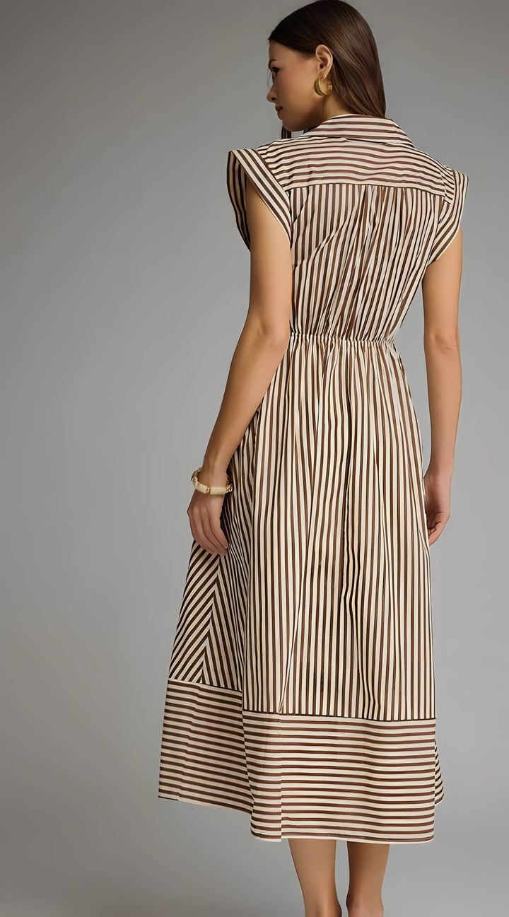 A woman shown from the back wearing a sleeveless midi dress with vertical brown and beige stripes, a high collar, and a gathered waist, photographed against a plain gray studio background.