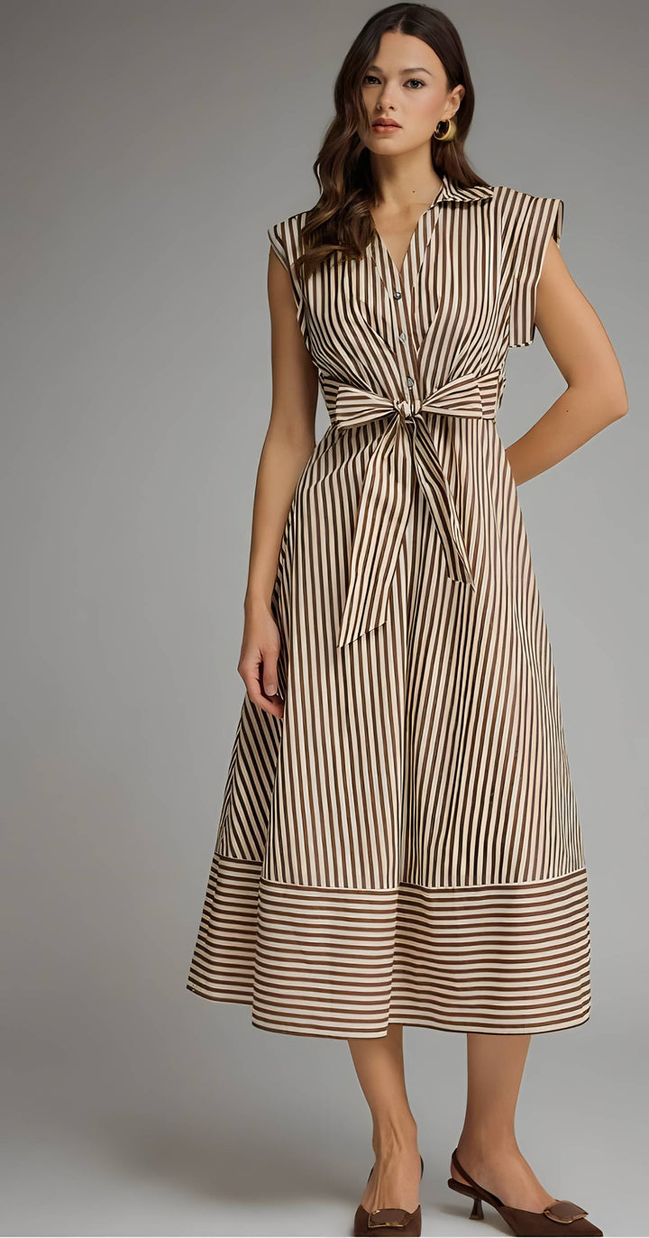 A woman models a sleeveless midi dress with vertical brown and beige stripes, featuring a tie-front waist and a tiered skirt, set against a solid gray studio background.