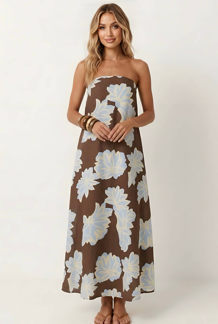 A woman modeling a strapless maxi dress with a brown base and large white floral print, standing against a plain light background.