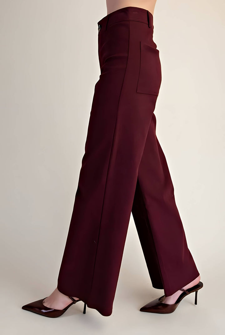 A person wearing high-waisted, wide-leg trousers in a deep burgundy or maroon shade, paired with dark brown pointed-toe heels, shown from the waist down against a plain light beige studio background.