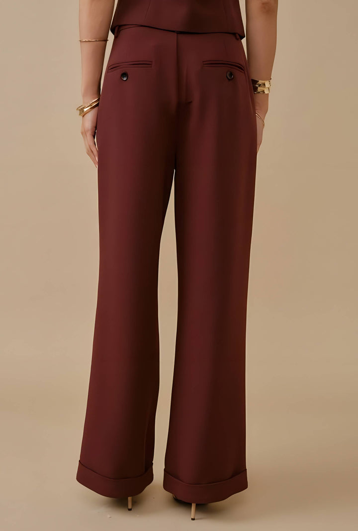 A person shown from the back wearing burgundy wide-leg trousers with a small button detail on the back pockets, paired with a matching top against a solid beige studio background.