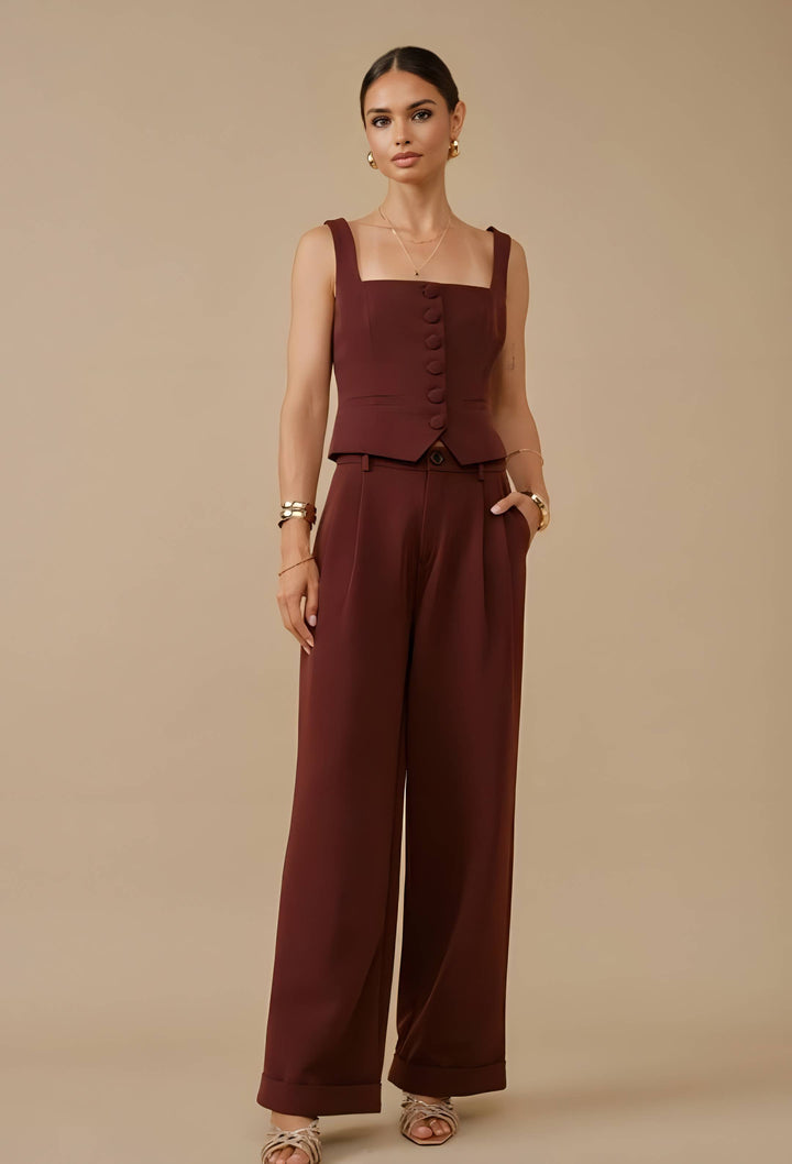 A woman modeling a sleeveless wide-leg jumpsuit in a deep burgundy color, standing against a solid beige studio background.