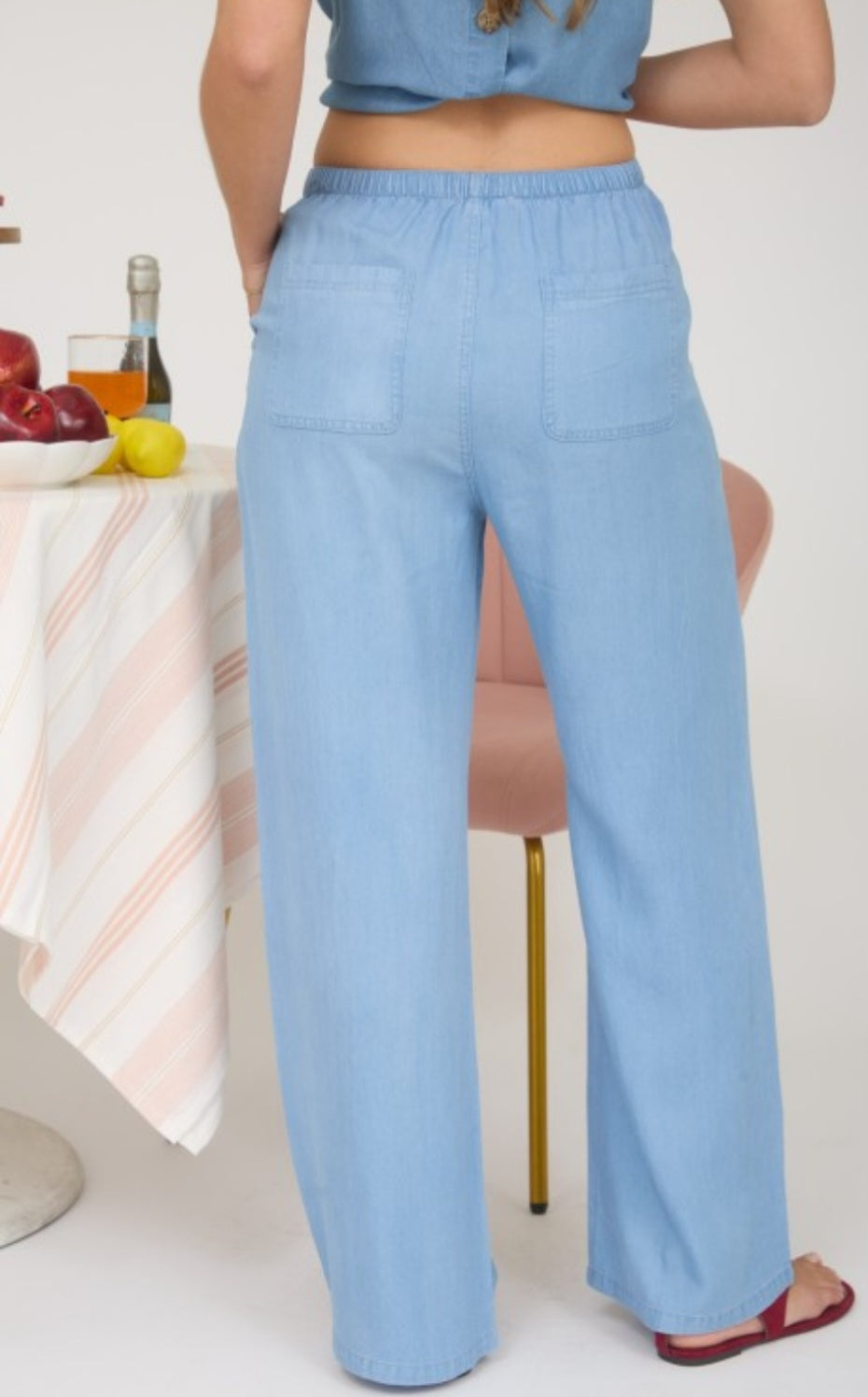Person wearing light blue pants sitting at a table with fruit and a bottle.