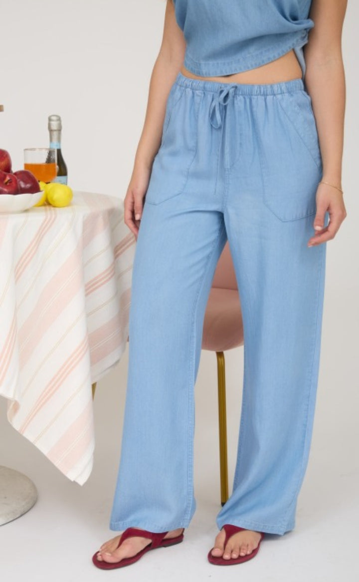Person wearing light blue pants sitting at a table with fruit and a bottle.