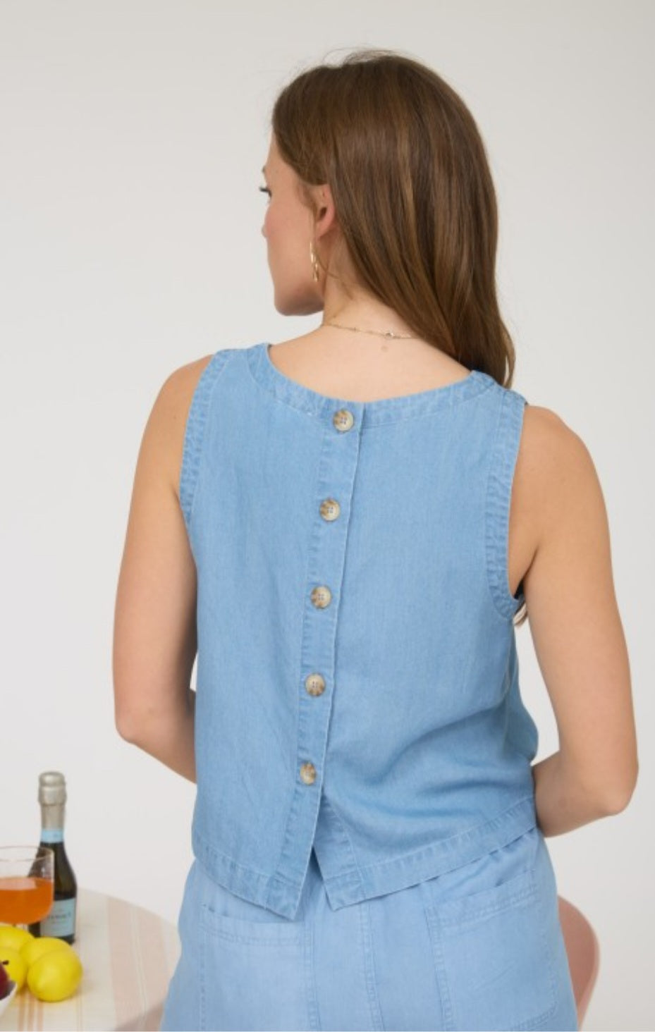 Woman wearing a light blue denim vest with buttons on a white background