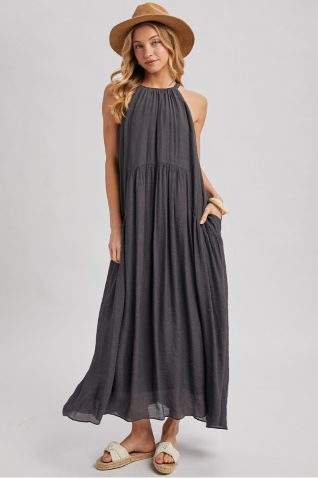 Woman wearing a long dark gray dress with a hat on a light gray background