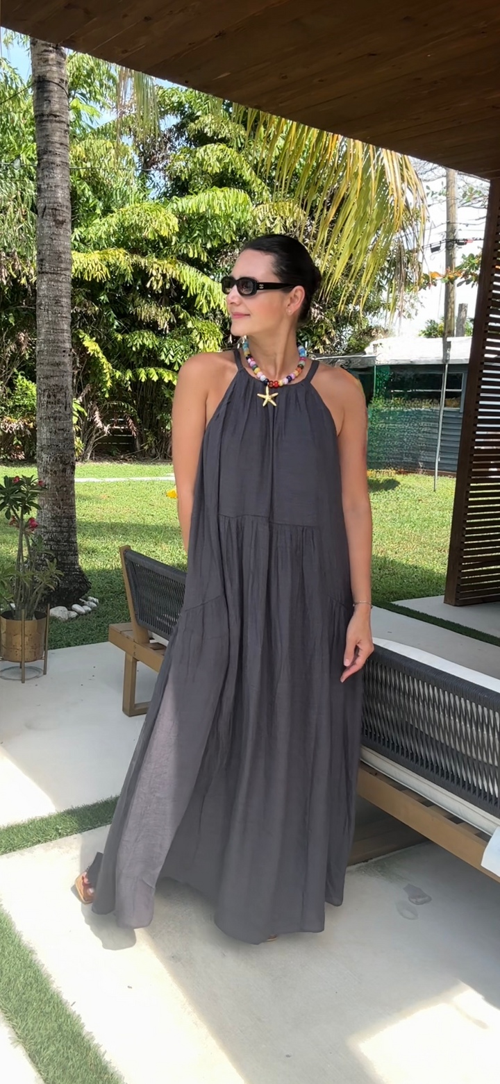 Woman in a gray dress standing outdoors with greenery and a wooden structure in the background